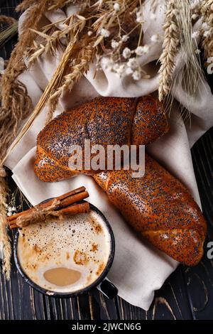 Fresh baked rolls with poppy seeds and coffee on rustic dark wooden table. Stock Photo