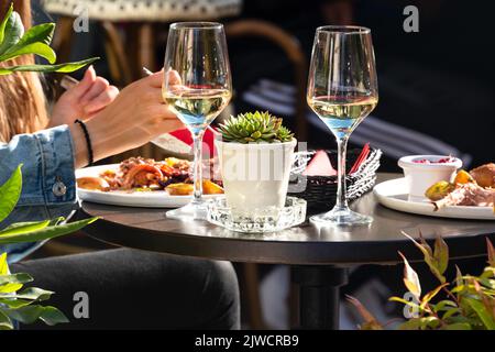 White wine and tasty dishes in outdoor restaurant. Couple having lunch or dinner in sunny summer day in sidewalk cafe. Friends having a meal outdoors Stock Photo