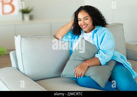 Happy African American Woman Sitting On Sofa At Home Stock Photo