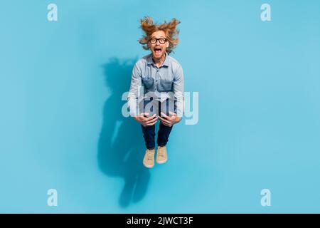Full length photo of impressed funky man wear denim shirt spectacles jumping diving isolated blue color background Stock Photo