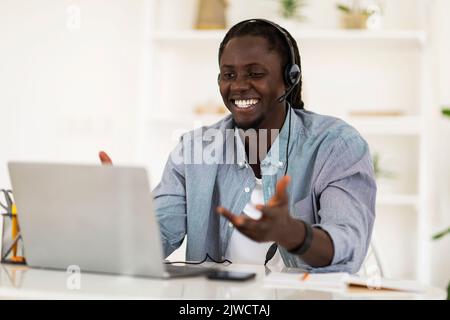 Smiling African American Guy In Headset Making Video Call With Laptop Stock Photo