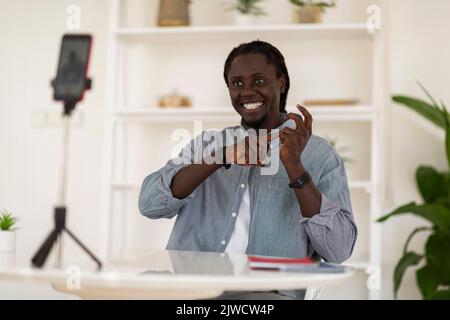 Cheerful black man broadcasting from home, using smartphone on tripod Stock Photo