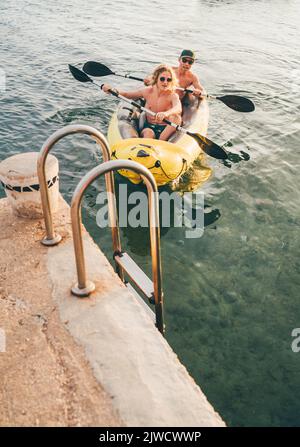 Father with teenager son on the bright yellow inflatable kayak returning back from evening ride by the Adriatic sea harbor in Croatia near from Sibeni Stock Photo