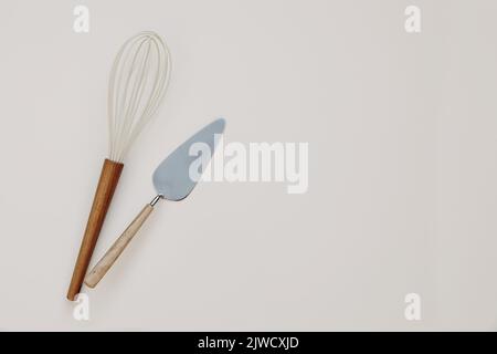 Elegant kitchen utensils, kitchenware. White silicon whisk and cake spoon with wooden handle isolated on beige table background. Baking, cooking Stock Photo