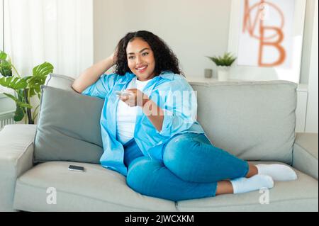 Black Woman Turning On TV With Remote Controller At Home Stock Photo