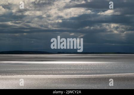 Moody landscape with dark clouds, dark sky and sunlight reflecting off the sea. View across Morecambe Bay from Canal Foot, Ulverston, Cumbria, UK Stock Photo