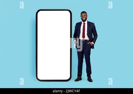 Successful Young Black Businessman In Suit Standing Near Huge Blank Smartphone Stock Photo