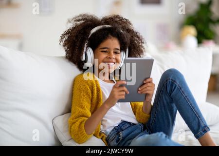 Happy kid sitting on couch, using digital tablet and headset Stock Photo