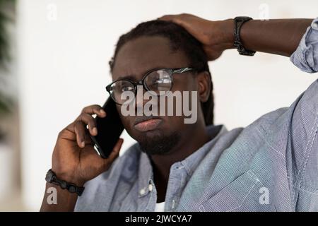 Stressed Black Male In Eyeglasses Touching Head While Talking On Cellphone Stock Photo