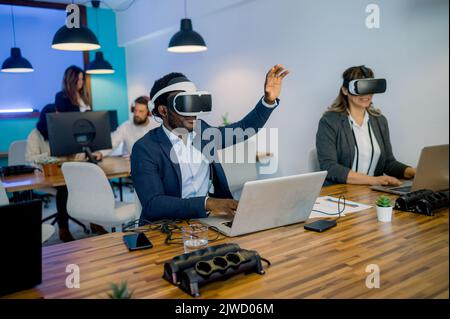 Multiracial colleagues in VR glasses using laptops in modern coworking space Stock Photo