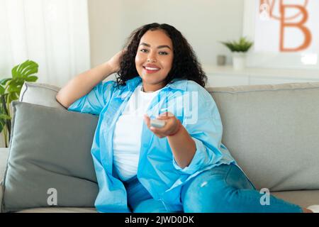 African American Lady Watching Television Pointing Remote Controller At Home Stock Photo