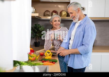 Happy Senior Couple Relaxing At Home, Cooking Healthy Food And Drinking Tea Stock Photo