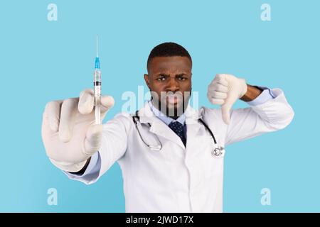 Displeased Black Male Doctor Holding Syringe And Showing Thumb Down Stock Photo