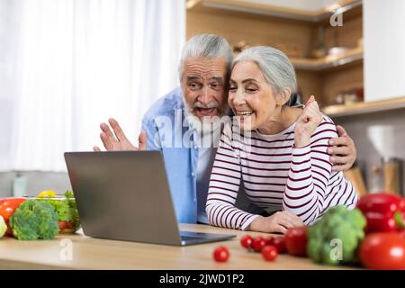 Happy Senior Couple Making Video Call With Laptop While Relaxing In Kitchen Stock Photo
