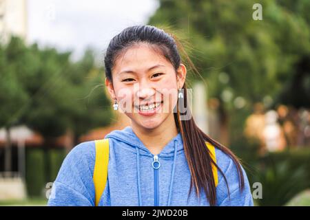 Young chinese lady student smiling looking at camera at the high school. Close up portrait of cute asian girl standing and laughing at campus. Stock Photo