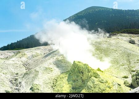 bright smoking fumarole with sulfur deposits against the background of the Mendeleev volcano peak on the island of Kunashir Stock Photo