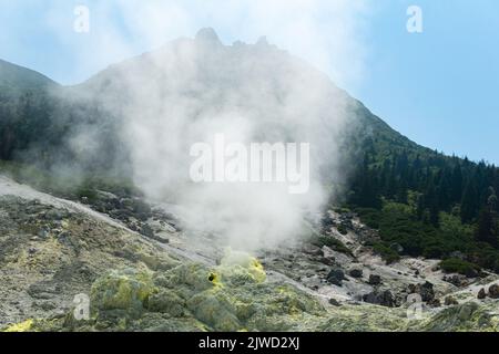 bright smoking fumarole with sulfur deposits against the background of the Mendeleev volcano peak on the island of Kunashir Stock Photo