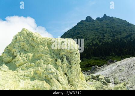 bright smoking fumarole with sulfur deposits against the background of the Mendeleev volcano peak on the island of Kunashir Stock Photo