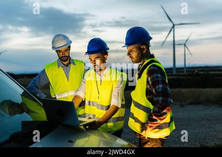 Engineers teamwork discussing renewable energy project at wind turbine farm Stock Photo
