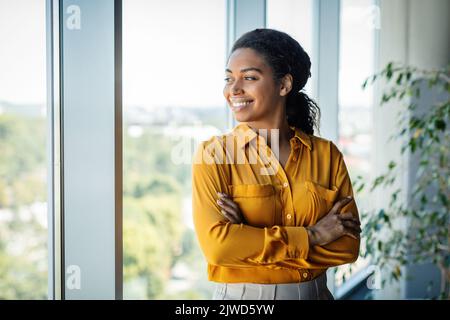 Portrait of confident african american businesswoman standing near window in modern company office, free space Stock Photo