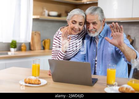 Happy senior spouses making video call with laptop in kitchen during breakfast Stock Photo