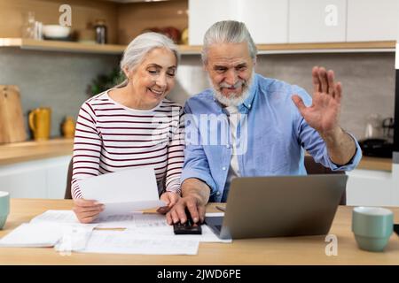Senior Spouses Making Video Call With Accountant While using Laptop In Kitchen Stock Photo