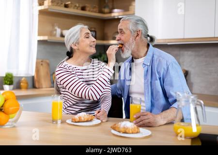 Romantic Senior Spouses Having Breakfast Together In Kitchen At Home Stock Photo