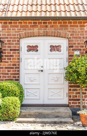 White front door with small square decorative windows and flower pots with red brick wall Stock Photo