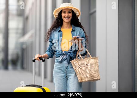 Cheerful young lady going vacation, walking by airport with suitcase Stock Photo