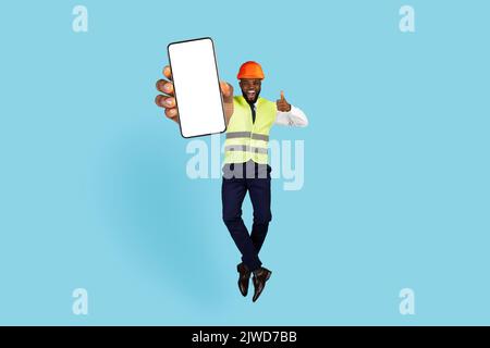 Black Engineer With Blank Smartphone In Hand Jumping And Showing Thumb Up Stock Photo