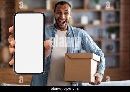 Delivery Service App. Excited black man holding box and showing blank smartphone Stock Photo
