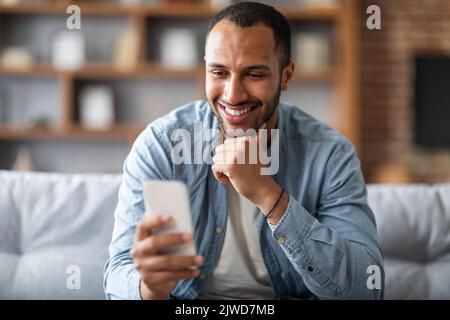 Handsome Young Black Man Looking At Smartphone In His Hand And Smiling Stock Photo