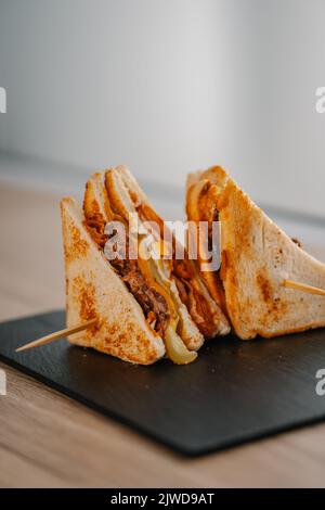 Yummy crispy sandwiches with meat, cheese, and pickles served on a black board Stock Photo