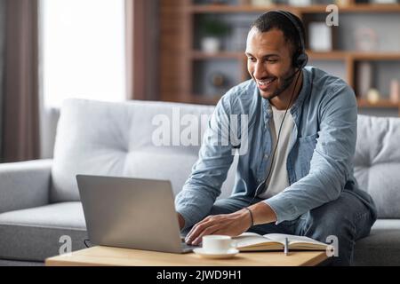 Distance Learning. Smiling Black Man In Headset Studying With Laptop At Home Stock Photo