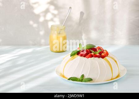 Pavlova cake with strawberries and lemon curd on a light sunny background. Homemade baking. Stock Photo