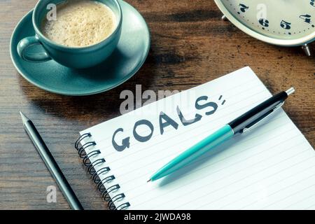 Goal setting. A notepad with the handwritten word on a desk, with a pen, an alarm clock, and a cup of coffee. The concept of resolutions and lists Stock Photo