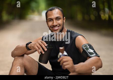 Happy african american sportsman sitting on the ground, having break Stock Photo