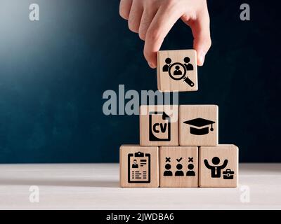 HRM, recruitment, job search and headhunting concept. Male hand holds wooden cube with icons of education, qualification, cv, resume, skills and exper Stock Photo