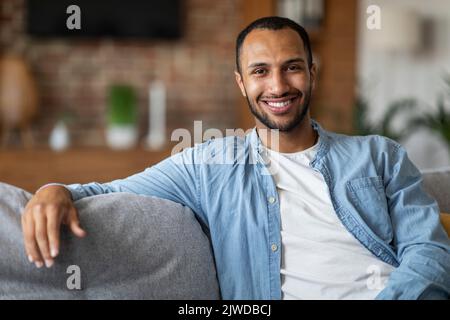 Portrait Of Smiling Young Black Man Posing On Couch At Home Stock Photo