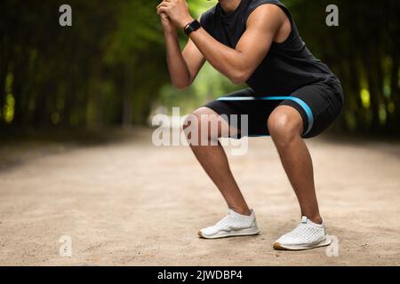 Unrecognizable muscular black man exercising in the park, using band Stock Photo