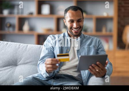 Online Payments. Handsome Black Young Man Using Digital Tablet And Credit Card Stock Photo