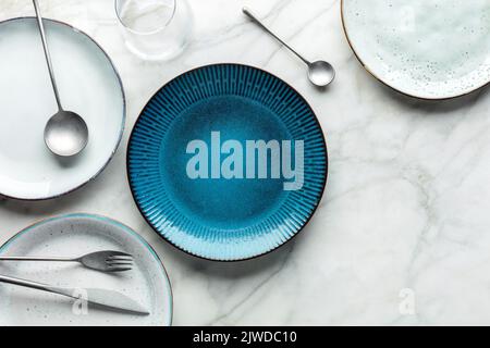 Modern tableware set with cutlery, a glass, and a vibrant blue plate, overhead flat lay shot with copy space. Trendy dinnerware Stock Photo