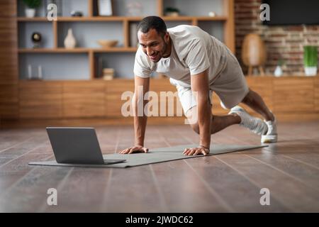 Online Training. Handsome Young Black Man Doing Sports At Home With Laptop Stock Photo