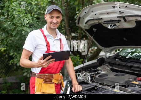 car service, repair, technology, maintenance and people concept - mechanic man with tablet pc computer making system diagnostic at workshop Stock Photo