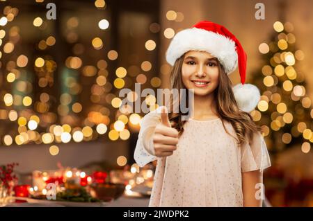 happy teenage girl in santa hat showing thumbs up Stock Photo