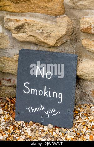 A 'No Smoking' sign painted on slate. The sign is propped up against a stone wall. Stock Photo