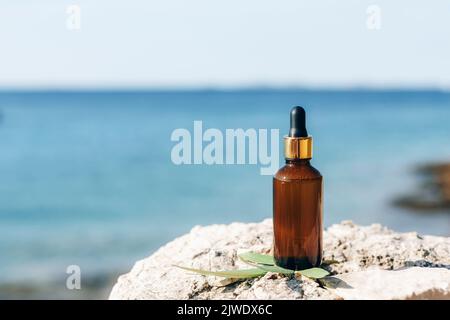 Glass bottle with oil or serum on the background of blue sea. Copy space Stock Photo