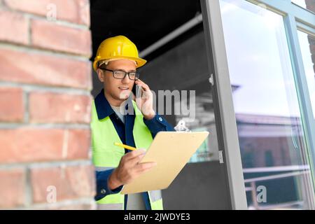 builder with clipboard and calling on smartphone Stock Photo