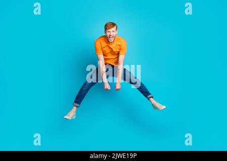 Full body photo of impressed ginger hair guy jump wear t-shirt jeans sneakers isolated on blue color background Stock Photo