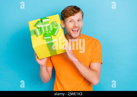 Photo of impressed ginger hair guy hold gift wear orange t-shirt isolated on teal color background Stock Photo